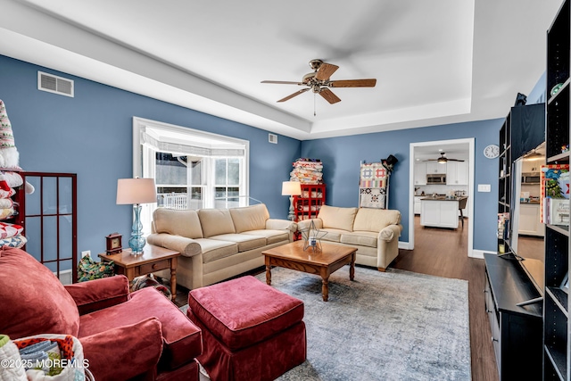 living room with baseboards, visible vents, a ceiling fan, wood finished floors, and a tray ceiling