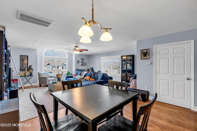 dining area with light wood-type flooring, baseboards, visible vents, and ceiling fan with notable chandelier