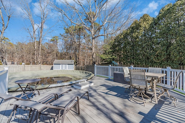 deck with a fenced backyard, a storage unit, outdoor dining area, and an outdoor structure