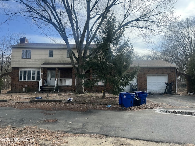 view of front of house featuring aphalt driveway, brick siding, a chimney, covered porch, and a garage