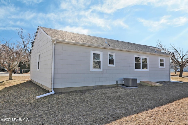 rear view of property featuring central air condition unit and a shingled roof