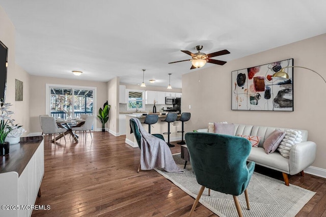 living area with dark wood-style floors, ceiling fan, and baseboards