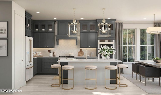 kitchen featuring light countertops, decorative backsplash, glass insert cabinets, an island with sink, and a kitchen breakfast bar