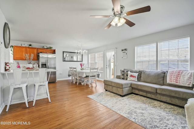 living room with light wood-type flooring, baseboards, and ceiling fan with notable chandelier