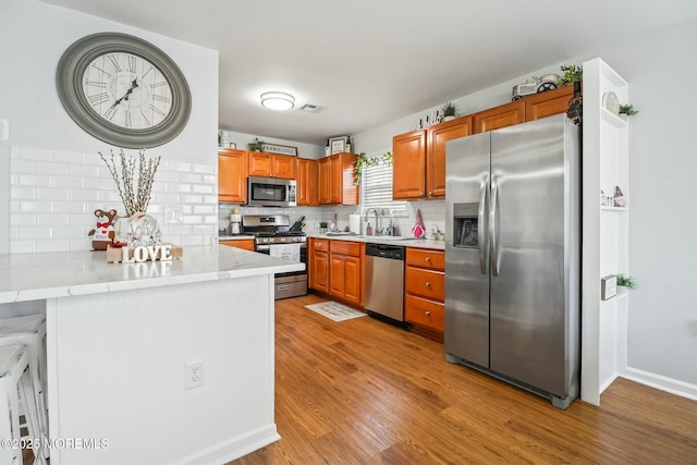 kitchen featuring light wood-style flooring, stainless steel appliances, a peninsula, tasteful backsplash, and brown cabinetry