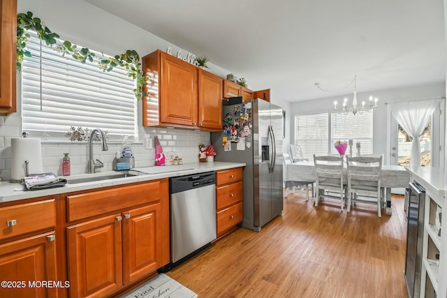 kitchen featuring light wood finished floors, tasteful backsplash, appliances with stainless steel finishes, light countertops, and a sink