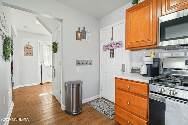 kitchen featuring backsplash, stainless steel appliances, light countertops, and wood finished floors