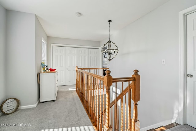 corridor with a chandelier, baseboards, an upstairs landing, and light colored carpet