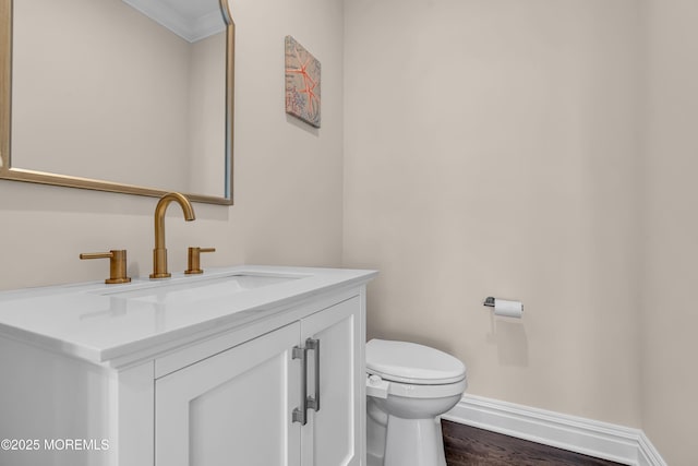 half bathroom with vanity, wood finished floors, baseboards, crown molding, and toilet