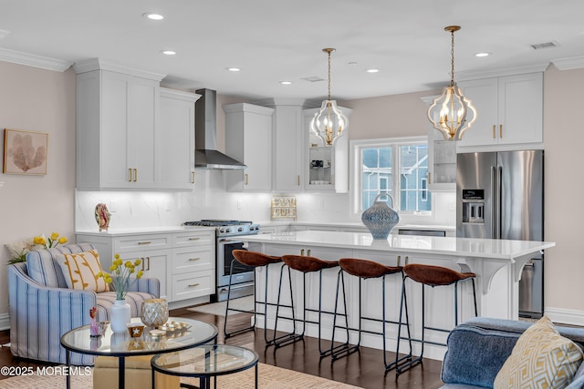 kitchen with a breakfast bar area, visible vents, a kitchen island, appliances with stainless steel finishes, and wall chimney exhaust hood