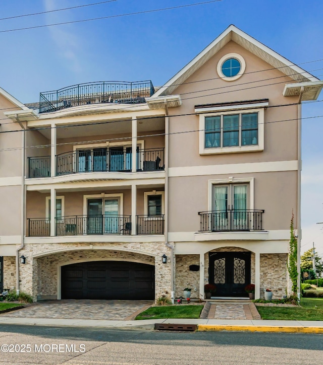 view of front facade with stucco siding, decorative driveway, stone siding, french doors, and a garage