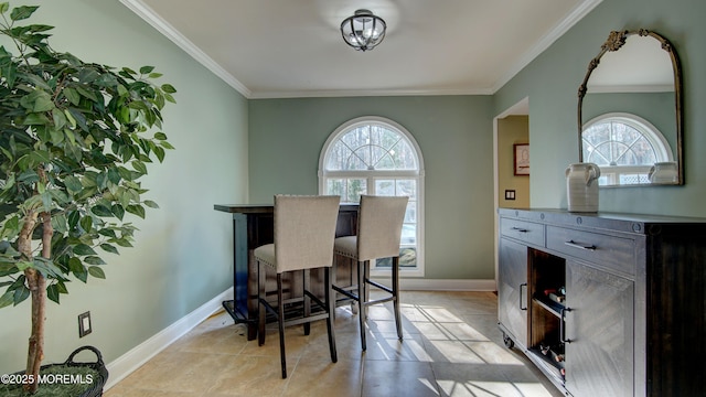 dining room featuring a bar, light tile patterned floors, baseboards, and crown molding