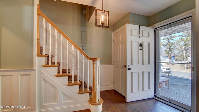 foyer entrance with dark wood finished floors, wainscoting, a decorative wall, and stairs