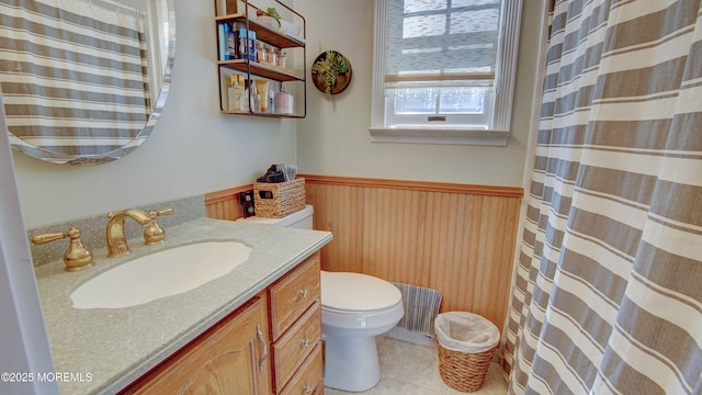 bathroom featuring toilet, a wainscoted wall, tile patterned flooring, vanity, and wood walls