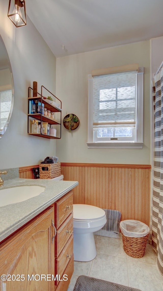 bathroom with wooden walls, wainscoting, toilet, tile patterned flooring, and vanity