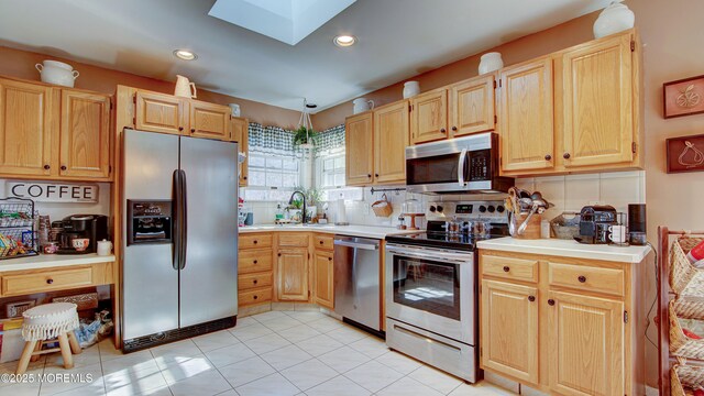 kitchen with a skylight, stainless steel appliances, light countertops, decorative backsplash, and light brown cabinets