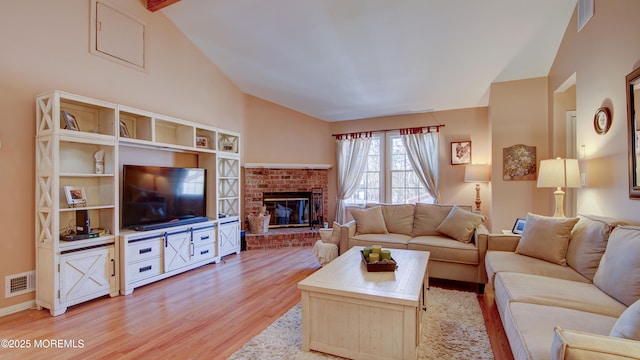 living area featuring vaulted ceiling, light wood-type flooring, a fireplace, and visible vents