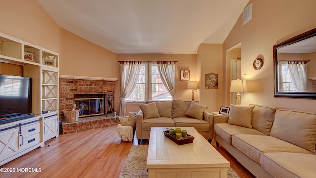 living area with light wood-style floors, vaulted ceiling, visible vents, and a fireplace