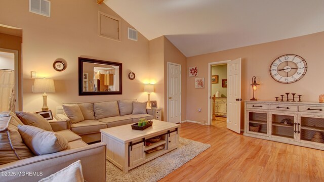 living area featuring high vaulted ceiling, light wood-style flooring, visible vents, and baseboards