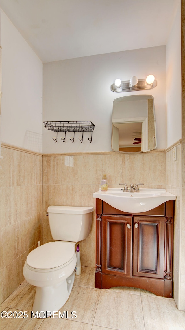 bathroom featuring tile patterned flooring, toilet, a wainscoted wall, vanity, and tile walls