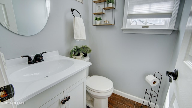 half bath featuring baseboards, vanity, toilet, and wood finished floors