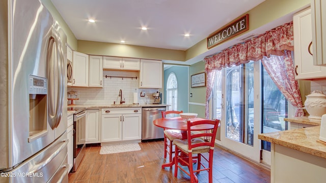 kitchen with stainless steel appliances, backsplash, light wood-style floors, white cabinetry, and a sink