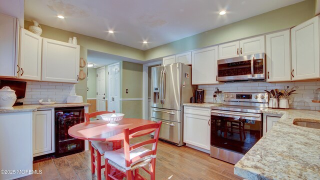 kitchen featuring white cabinets, beverage cooler, stainless steel appliances, and light wood-style flooring