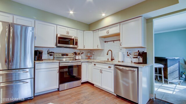 kitchen featuring stainless steel appliances, white cabinets, a sink, and backsplash