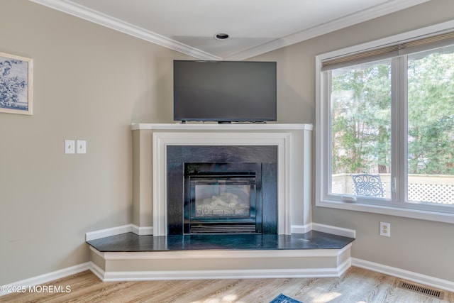 details featuring visible vents, crown molding, baseboards, wood finished floors, and a glass covered fireplace