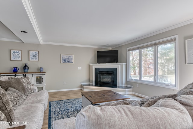 living area with a glass covered fireplace, wood finished floors, baseboards, and ornamental molding