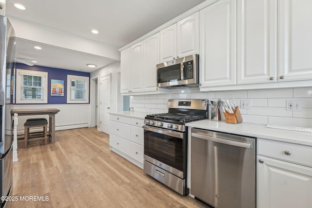 kitchen with a baseboard heating unit, white cabinets, light wood-style floors, light countertops, and appliances with stainless steel finishes