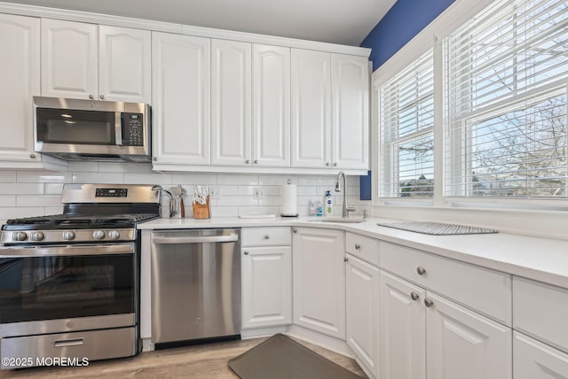 kitchen featuring tasteful backsplash, white cabinetry, stainless steel appliances, and a sink