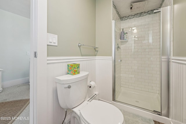 bathroom featuring toilet, a stall shower, and wainscoting