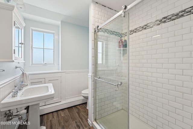 bathroom featuring a shower stall, wood tiled floor, a baseboard heating unit, and wainscoting