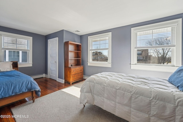 bedroom with baseboard heating, visible vents, baseboards, and wood finished floors