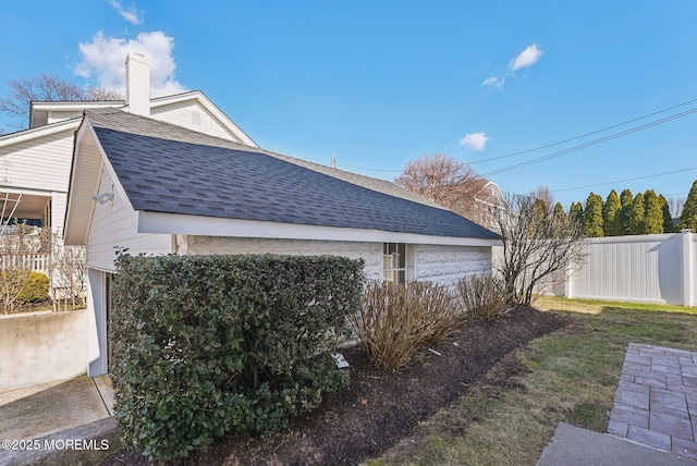 view of side of home with a detached garage, a chimney, a shingled roof, fence, and an outdoor structure