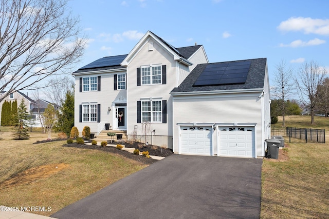 view of front facade with a front lawn, driveway, roof mounted solar panels, fence, and a garage