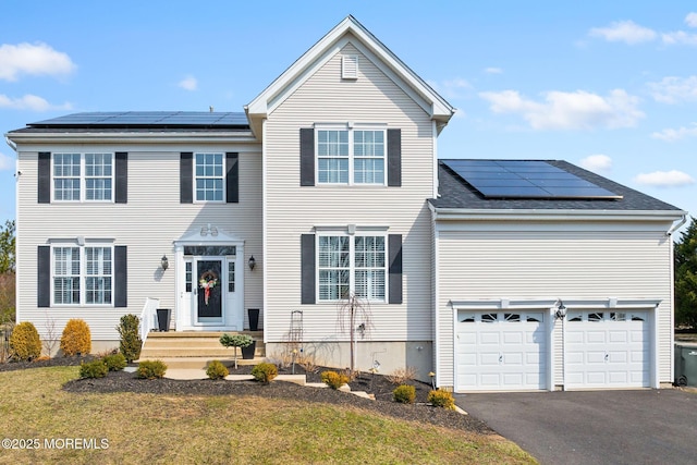 traditional home with roof mounted solar panels, an attached garage, roof with shingles, and driveway