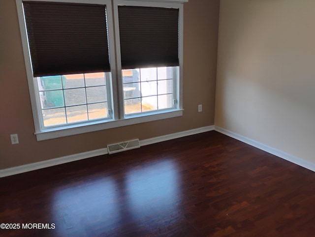 empty room with dark wood-style flooring, visible vents, and baseboards