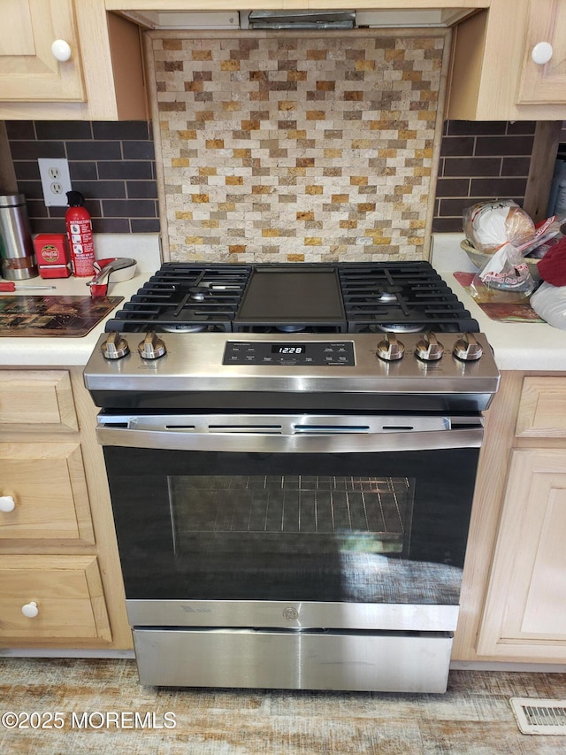 kitchen with gas range, light brown cabinets, light countertops, and backsplash