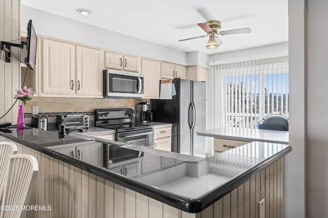 kitchen featuring ceiling fan, a breakfast bar area, a peninsula, appliances with stainless steel finishes, and backsplash