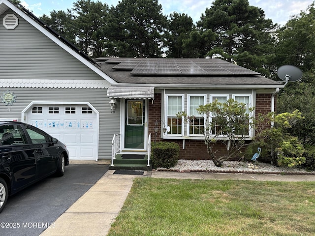 view of front of home featuring driveway, brick siding, an attached garage, and roof mounted solar panels