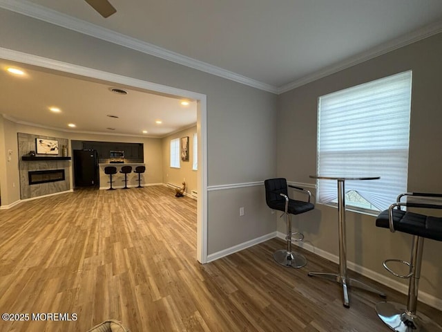 workout room featuring baseboards, a tiled fireplace, light wood-style flooring, ornamental molding, and recessed lighting