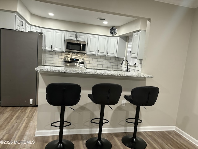 kitchen featuring a peninsula, appliances with stainless steel finishes, decorative backsplash, and wood finished floors