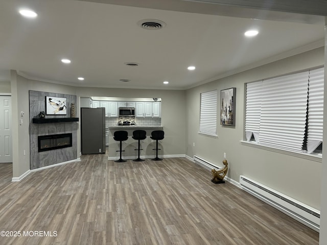 interior space with light wood-style floors, a baseboard radiator, visible vents, and ornamental molding