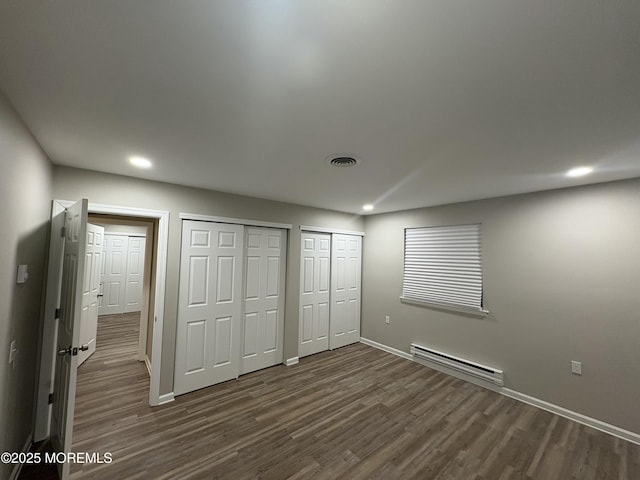 unfurnished bedroom featuring a baseboard radiator, two closets, visible vents, baseboards, and dark wood finished floors