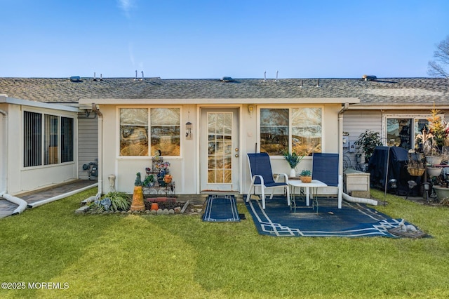 back of house featuring roof with shingles, a lawn, and a patio