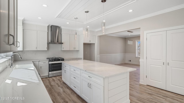 kitchen with light wood-style floors, a wainscoted wall, stainless steel range with gas stovetop, wall chimney range hood, and a sink