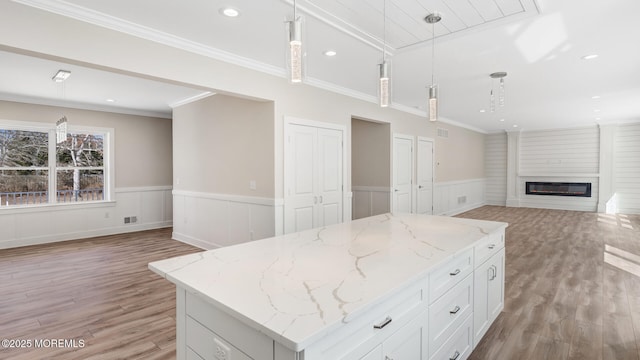 kitchen featuring open floor plan, a large fireplace, hanging light fixtures, and a wainscoted wall