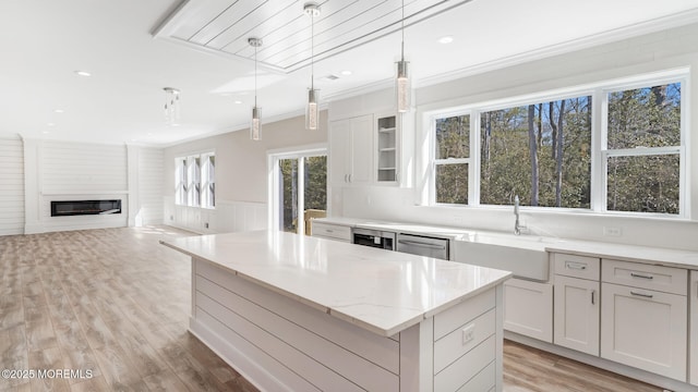 kitchen featuring light stone counters, a kitchen island, a sink, ornamental molding, and a glass covered fireplace